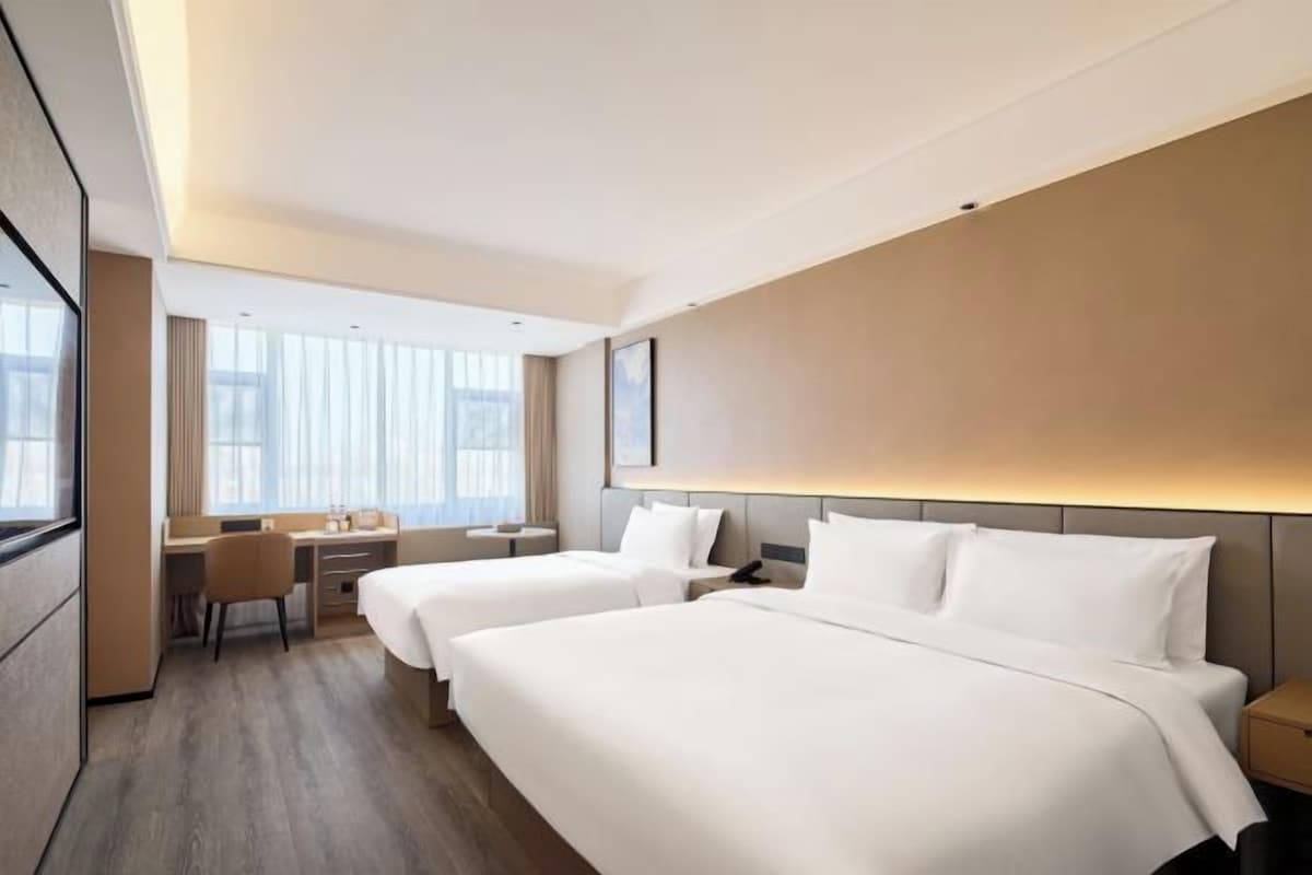 Habitació d'hotel amb dos llits, una taula de treball i una finestra gran.