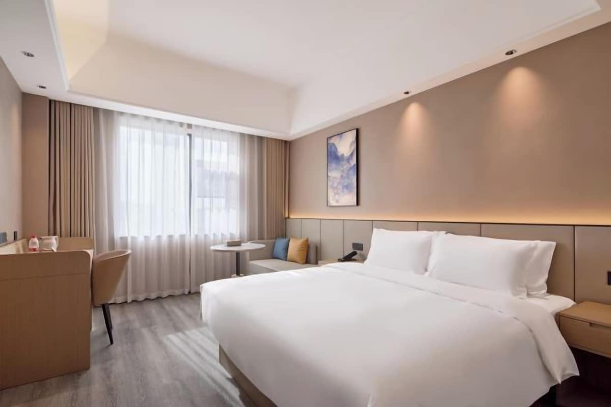 Una habitació d'hotel amb un llit gran, una escriptori, una cadira, una taula petita i una finestra amb cortines.