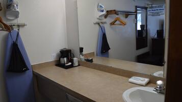 A bathroom with a sink, mirror, and hanging clothes rack.
