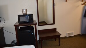 Een hotelkamer met een magnetron op een tafeltje, een bankje, een spiegel en een kapstok.