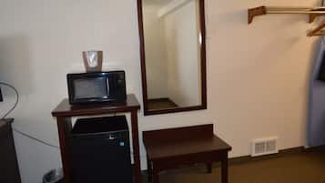 A hotel room with a microwave on a small table, a bench, a mirror, and a coat rack.