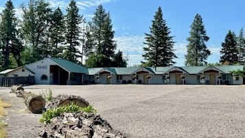 A motel with multiple buildings, a gravel parking area, and surrounding tall trees.