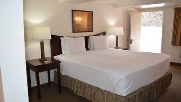 A hotel room with a large bed, two bedside tables with lamps, a framed picture on the wall, and a door leading to a balcony.