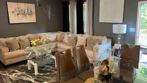 A modern living room with a sectional sofa, a glass coffee table with decorative items, and a ceiling fan. - Meadowstone Luxe Stay - 5star Comfort  (Atlanta)