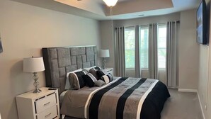 A bedroom with a large bed, a nightstand, a ceiling fan, and a window with curtains. - Meadowstone Luxe Stay - 5star Comfort  (Atlanta)