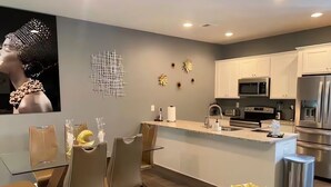A modern kitchen with white cabinets, a central island, stainless steel appliances, and a dining area with a glass table and chairs. - Meadowstone Luxe Stay - 5star Comfort  (Atlanta)