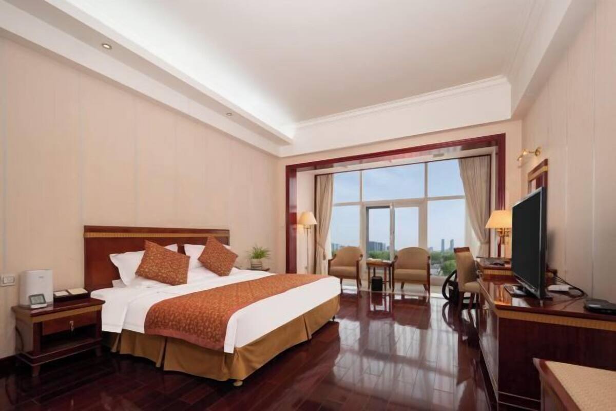 A hotel room with a large bed, a desk with a computer, a TV, and a view of the city.