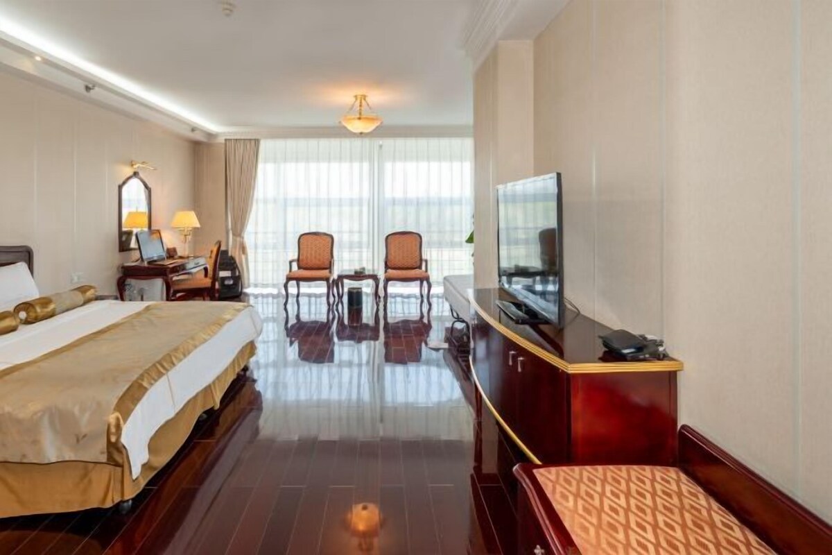 A hotel room with a bed, a desk with a computer, two chairs, a television, and a large window.