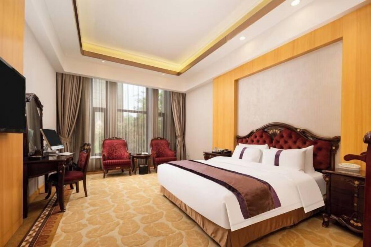 A hotel room with a large bed, a desk with a computer, two chairs, and a TV.