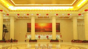 Un vestíbulo amplio con un gran emblema circular en el suelo, techos altos con iluminación decorativa y una pared central con un mural de atardecer.