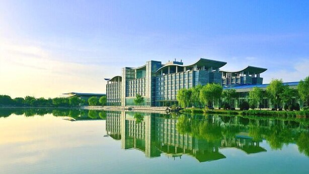 Un hotel moderno con su reflejo en el agua, que destaca por su amplia fachada de vidrio y un diseño arquitectónico único.