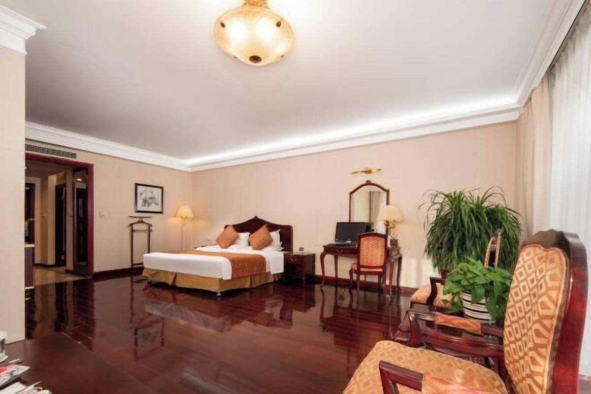 A hotel room with a bed, desk, chair, lamp, and potted plant.