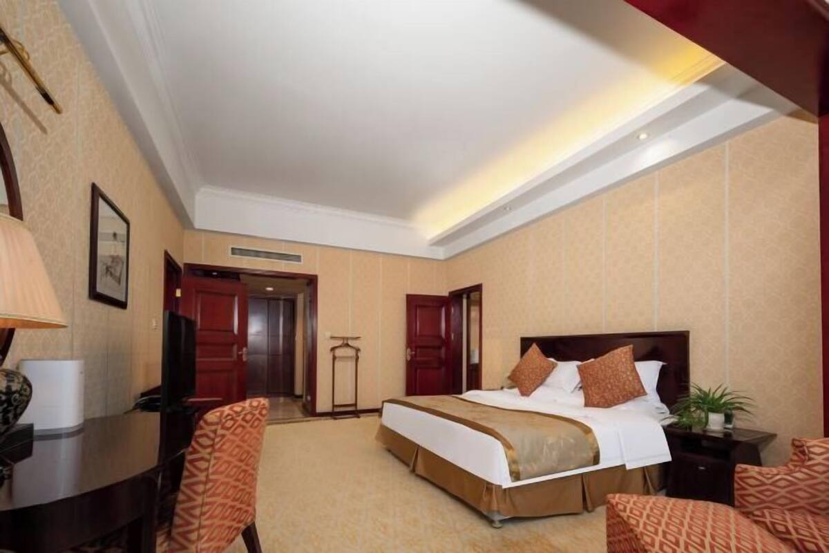 A hotel room with a large bed, a desk, a chair, and a small table.