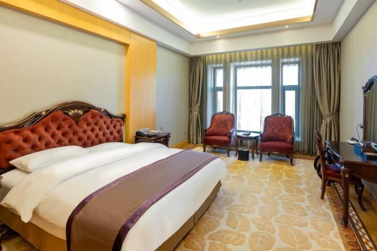 A hotel room with a large bed, two armchairs, a small table, and a desk.