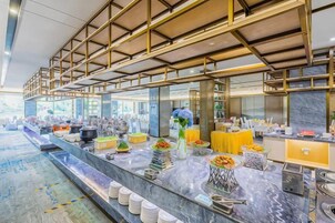 Zona de bufé con encimera de mármol, diferentes opciones de comida y un diseño moderno con detalles dorados.