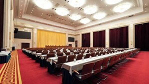 Un amplio salón de conferencias con filas de mesas y sillas, una alfombra roja y un escenario con cortinas.