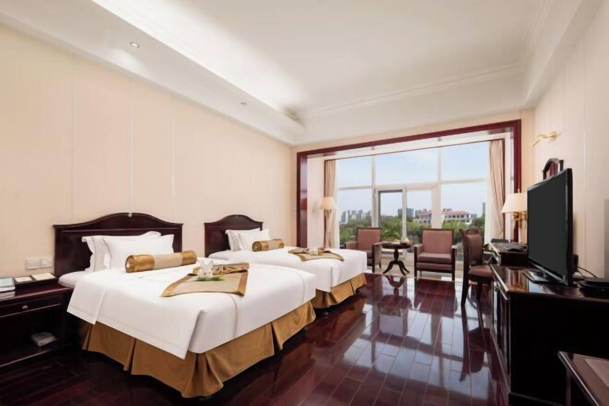 A hotel room with two beds, a TV, a desk, and a view of the city.