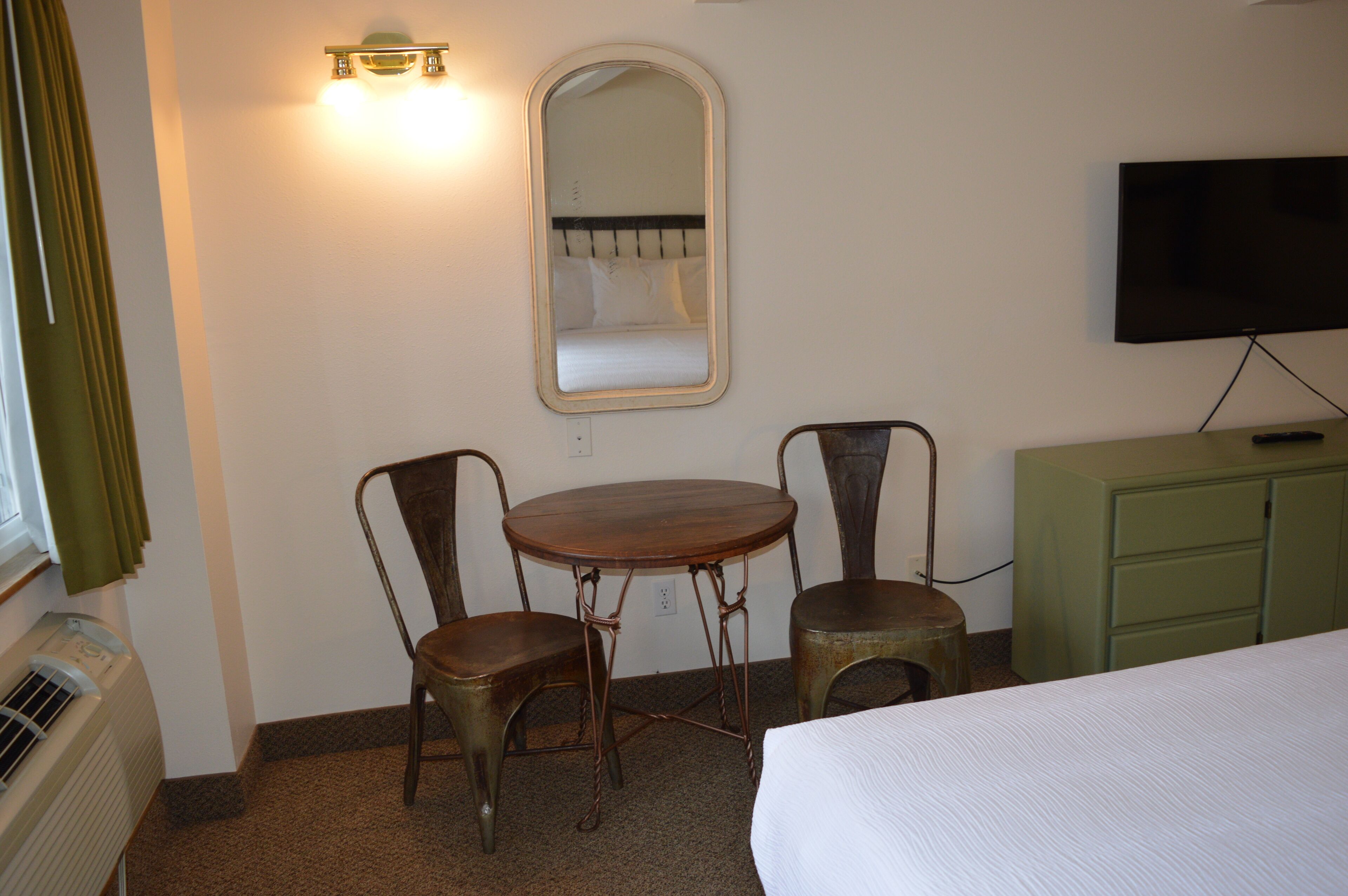 Ein Hotelzimmer mit einem Bett, einem Tisch, zwei Stühlen, einem Spiegel, einem Fernseher und einem grünen Schrank.