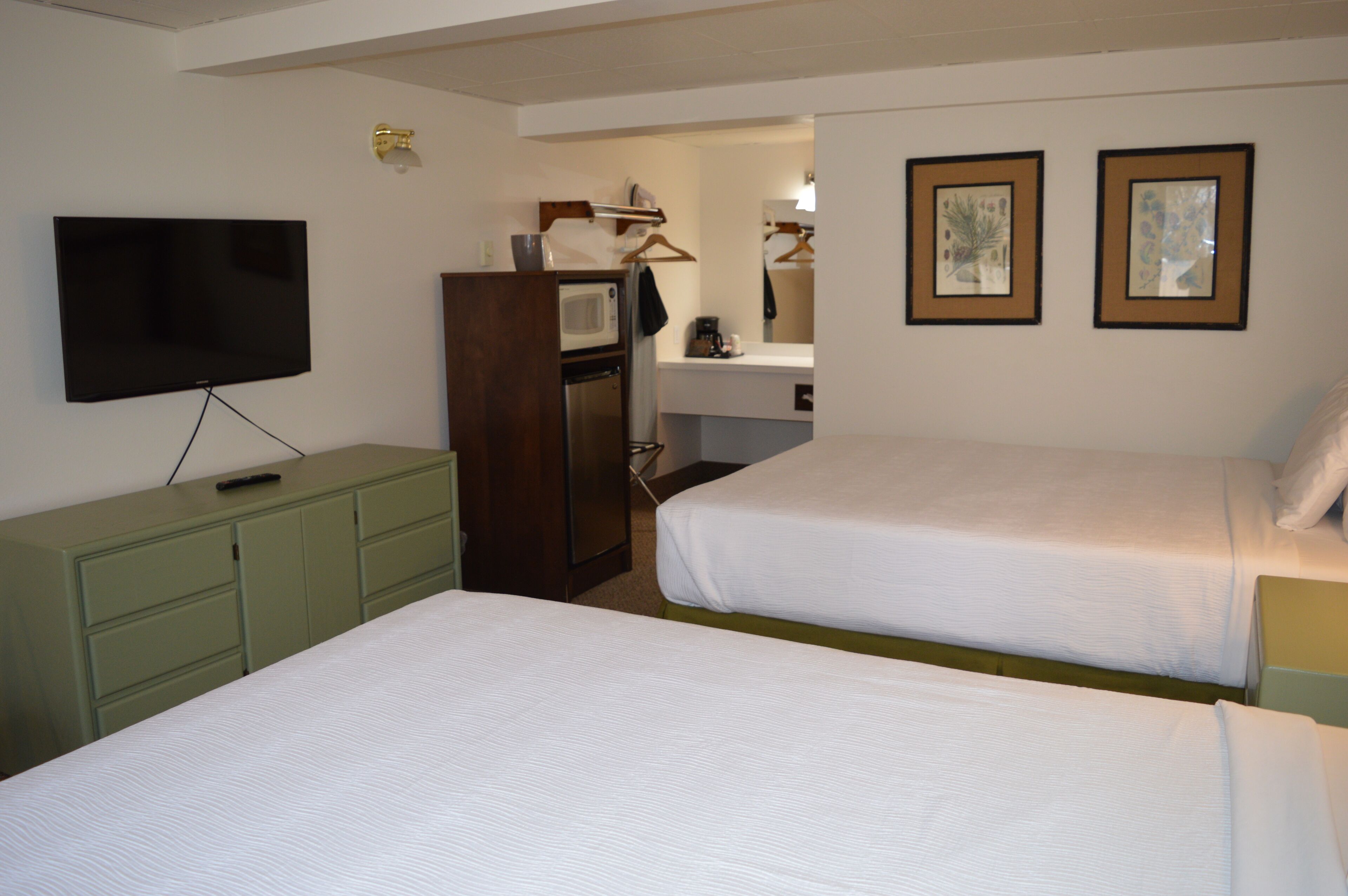 Ein Hotelzimmer mit zwei Betten, einem Fernseher, einer Mikrowelle, einer Kaffeemaschine und gerahmten Bildern an der Wand.