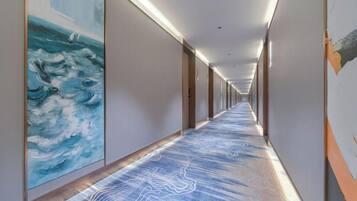 A long corridor with a patterned carpet, artwork on the walls, and doors on the right.