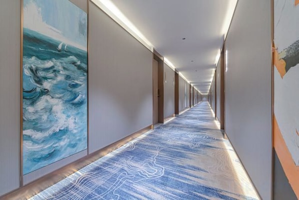 A long corridor with a patterned carpet, artwork on the walls, and doors on the right.