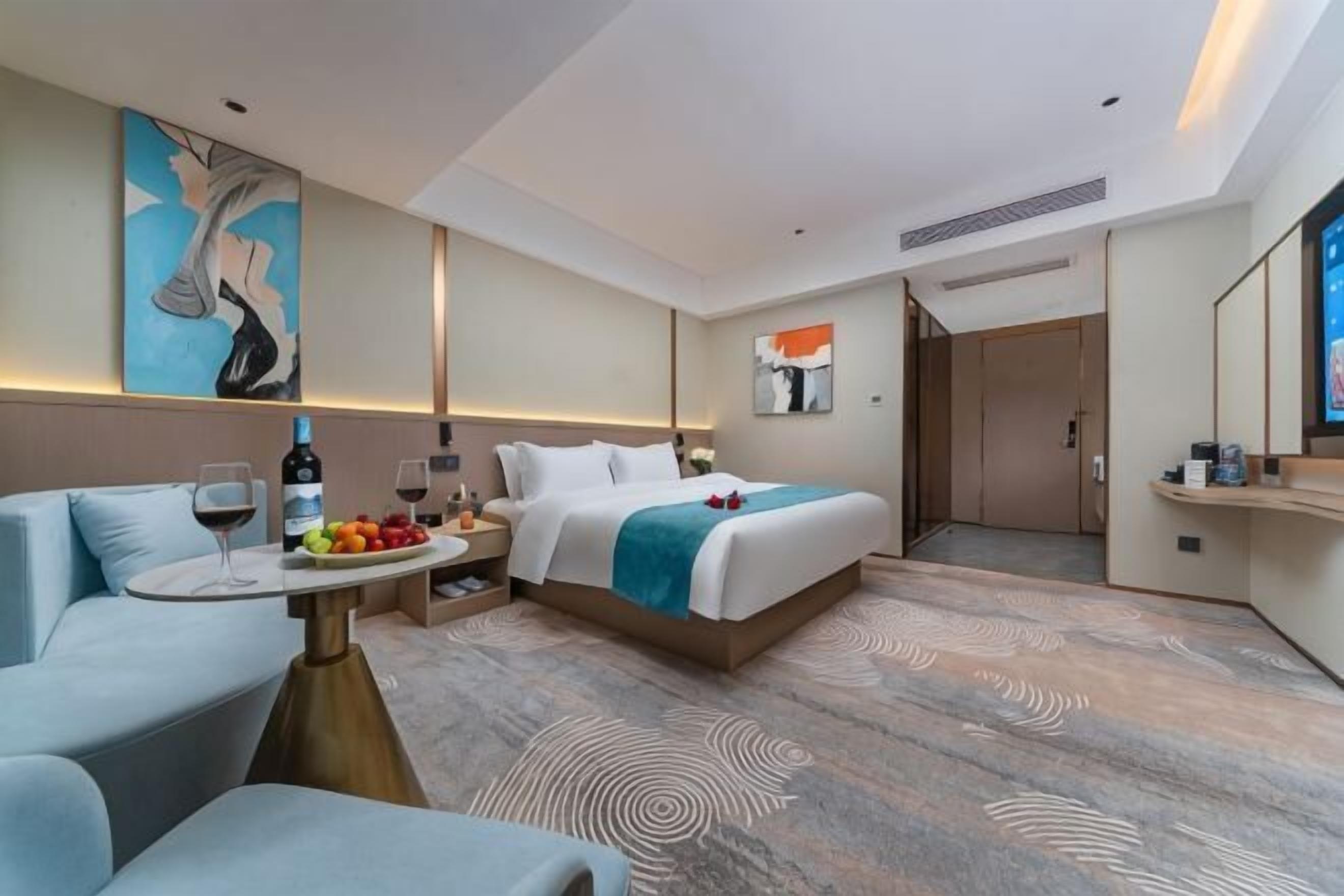 A hotel room with a bed, a sofa, a small table with a bottle and fruit, and a television.