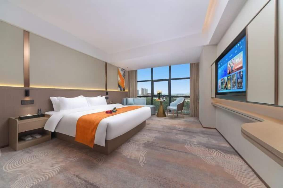 Une chambre d’hôtel moderne dotée d’un grand lit, d’une télévision, d’un bureau et d’un balcon offrant une vue sur la ville.