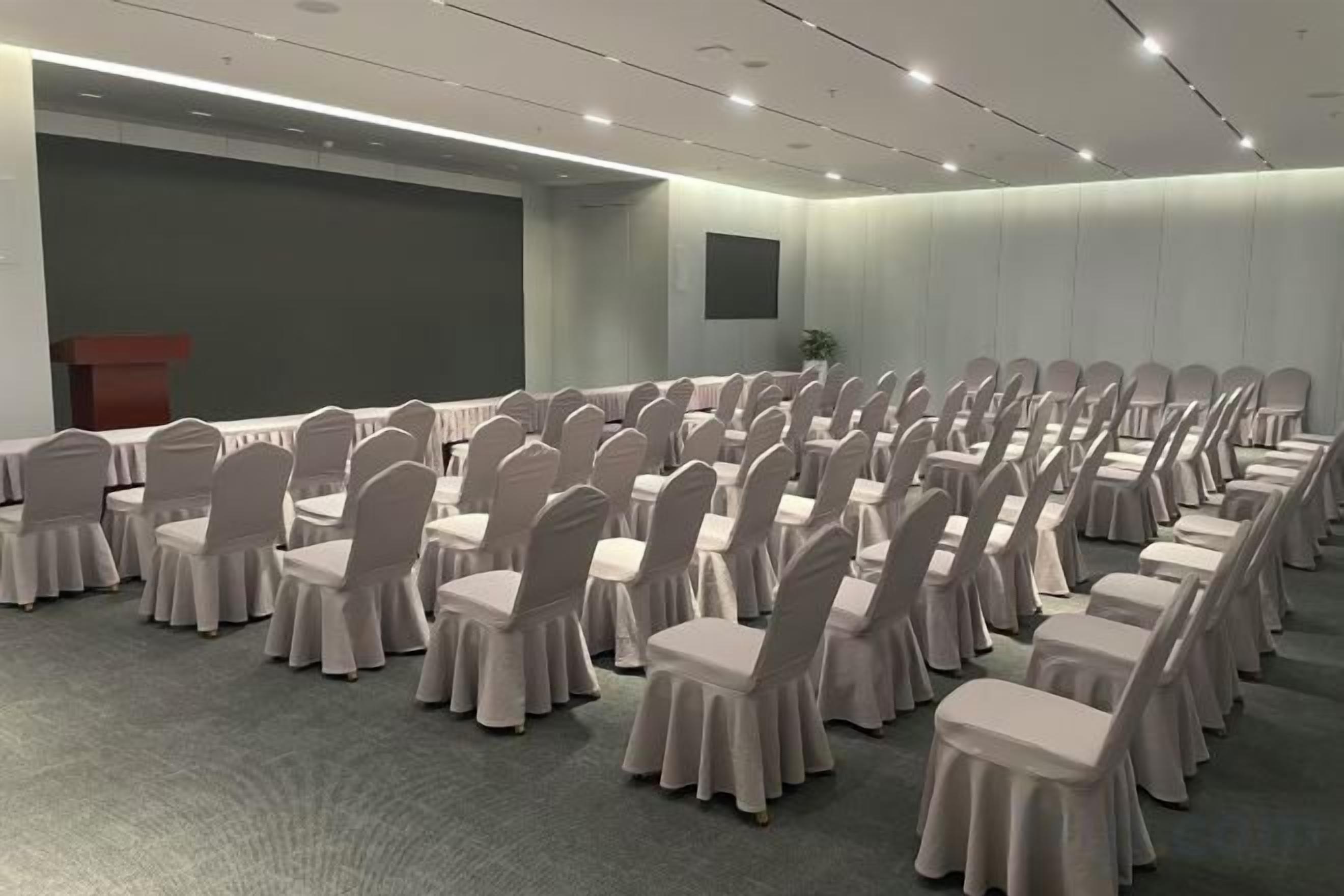 A conference room with rows of chairs and tables, a podium, and a neutral color scheme.