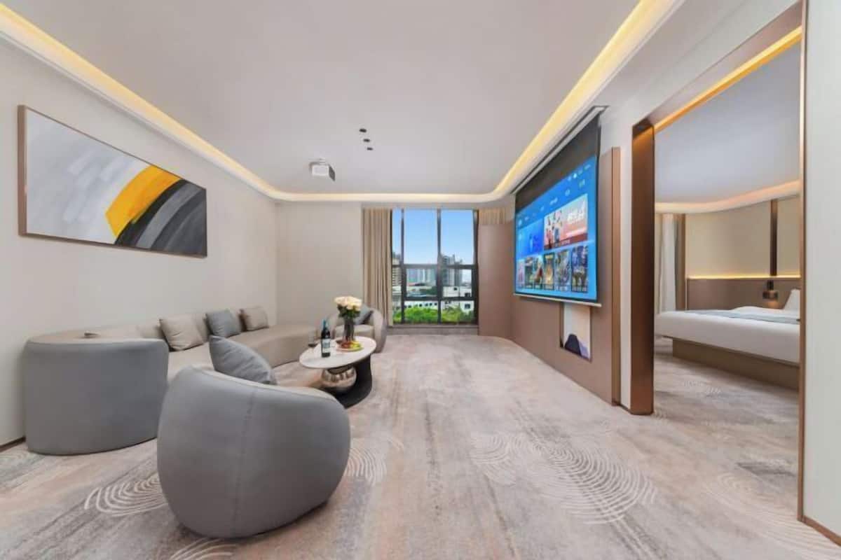 Une chambre d’hôtel moderne, dotée d’un canapé, d’un pouf et d’un téléviseur à écran plat fixé au mur.