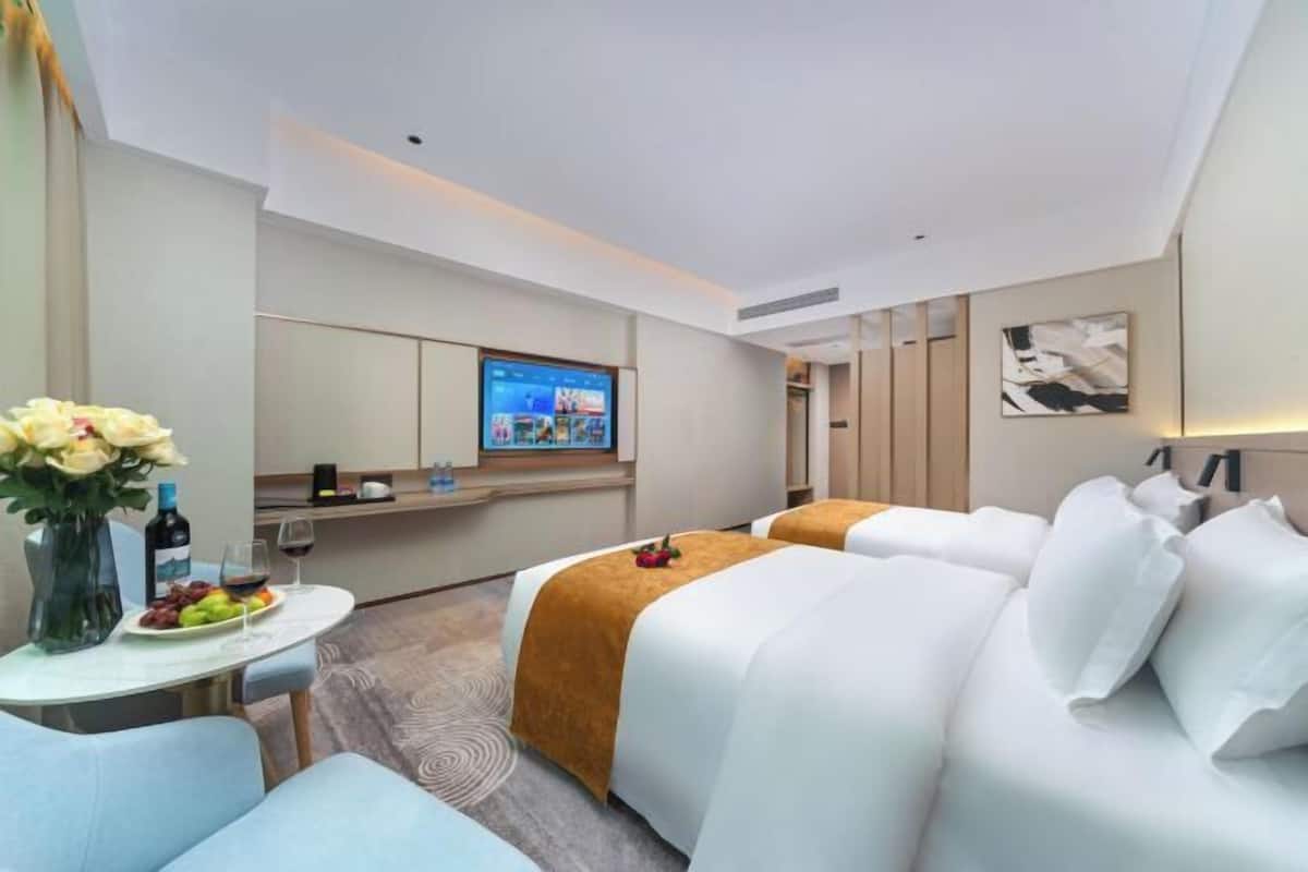 Une chambre d’hôtel moderne avec un lit, une télévision, une table à manger avec des fruits et un vase de fleurs.