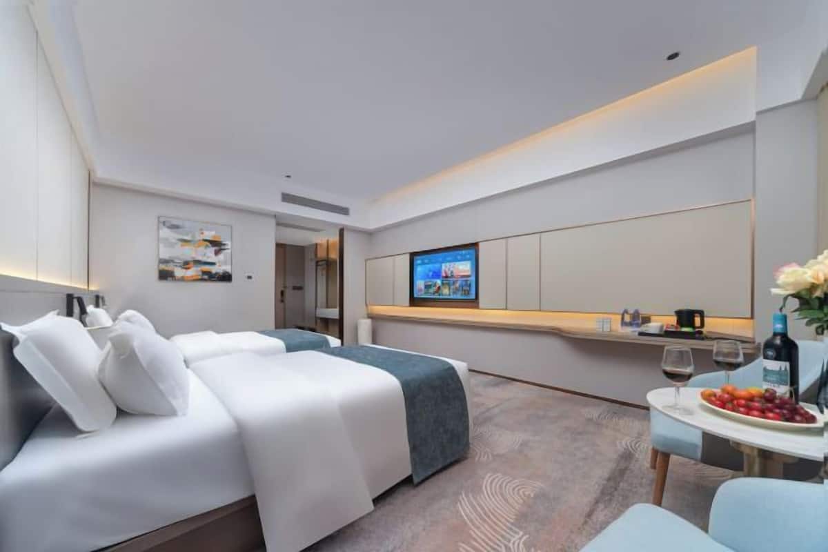 Une chambre d’hôtel moderne avec un lit, une petite table sur laquelle sont disposés des fruits et une bouteille de vin, une télévision et un grand miroir.