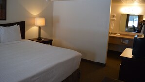 Une chambre d’hôtel avec un grand lit, une table de chevet avec une lampe, une salle de bain avec un miroir et un bureau avec un ordinateur.