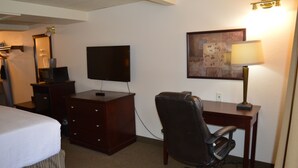 Une chambre d’hôtel comprenant un lit, un bureau, une chaise, une télévision, une lampe et un tableau au mur.