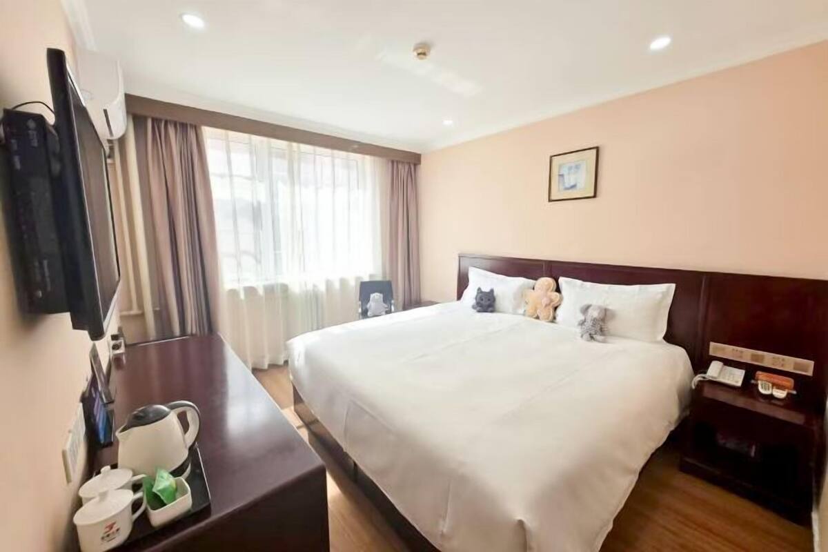 Une chambre d’hôtel avec un lit, une table de chevet, une télévision, une fenêtre avec des rideaux et un tableau au mur.