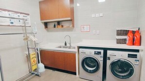 A laundry room with two washing machines, a sink, wooden cabinets, and a caution sign. - Jintai Home (Beijing North Railway Station Jiaotong University Branch) (Beijing)
