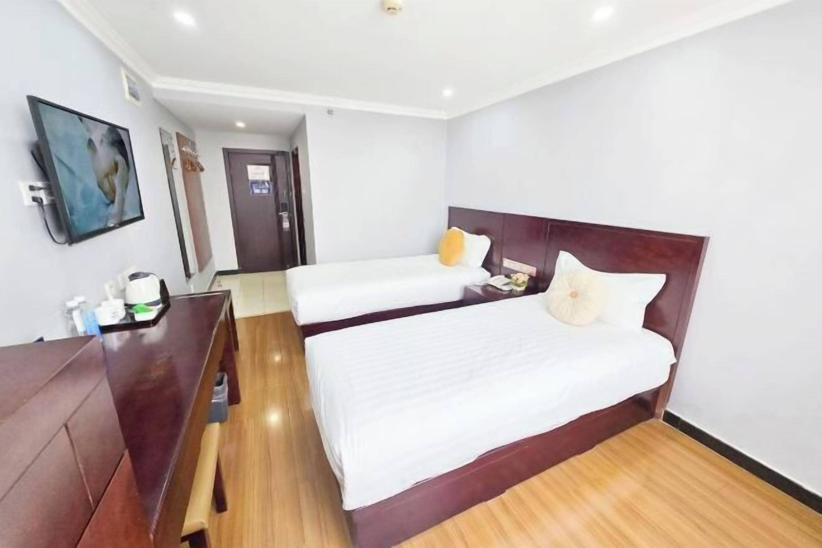 Habitación de hotel con dos camas, un escritorio de madera, un televisor y una puerta que da a otra habitación.