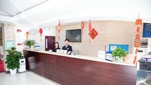 A hotel reception desk with a flat-screen TV, red decorations, and potted plants. - Jintai Home (Beijing North Railway Station Jiaotong University Branch) (Beijing)