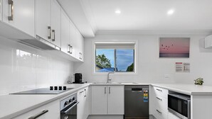 A modern kitchen with white cabinets, a built-in oven, a dishwasher, and a window with a view of the sky. - Wolaroi Villa 2, with Netflix and Disney Plus - In a Quiet Street (Orange)