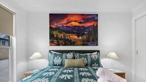 A bedroom with a bed, two bedside lamps, a painting of a mountain landscape, and a window with a view. - Wolaroi Villa 2, with Netflix and Disney Plus - In a Quiet Street (Orange)