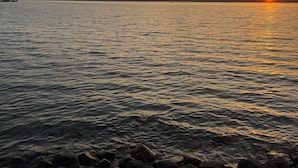 A sunset over a calm body of water with a rocky shoreline. - Torch Lake Farmhouse (Alden)
