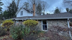 A stone house with a chimney, surrounded by a garden with various plants and a stone wall. - Torch Lake Farmhouse (Alden)