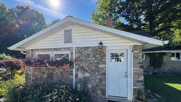 A stone house with a white door, a small porch with potted plants, and a well-maintained garden. - Torch Lake Farmhouse (Alden)