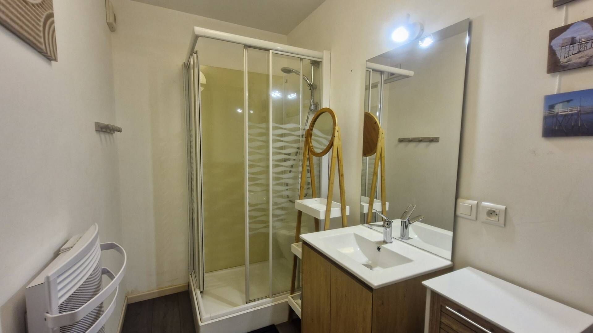 Een moderne badkamer met een glazen douchecabine, een houten wastafelmeubel en een grote spiegel.