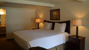 A hotel room with a large bed, two bedside tables with lamps, a painting on the wall, and a door to the left. - #25- ONE KING BED hotel with WiFi, AC in fabulous Columbia Falls. 20 mi to GNP (Columbia Falls)