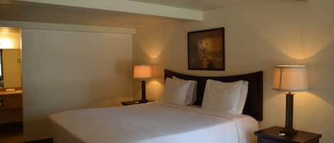 A hotel room with a large bed, two bedside tables with lamps, a painting on the wall, and a door to the left.