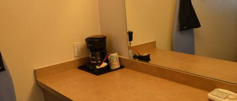 A hotel bathroom with a sink, mirror, towel dispenser, and a coffee maker.