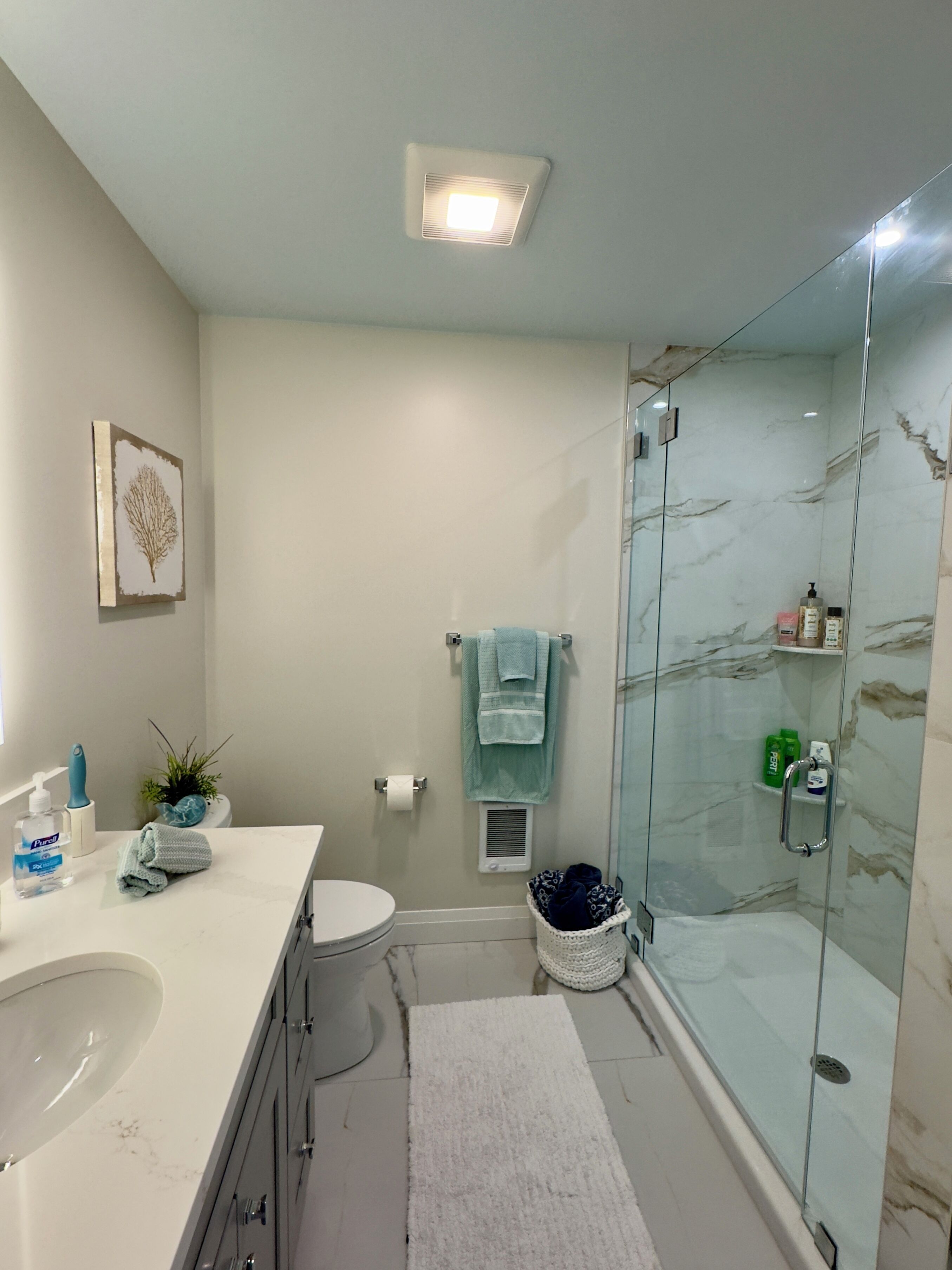 Un baño con un lavamanos blanco, inodoro, cabina de ducha de vidrio y un perchero para toallas.