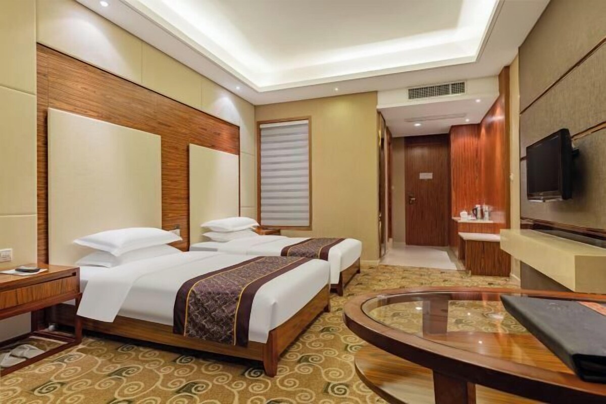 Ein Hotelzimmer mit zwei Betten, einem Fernseher, einem Schreibtisch und einem Badezimmer.