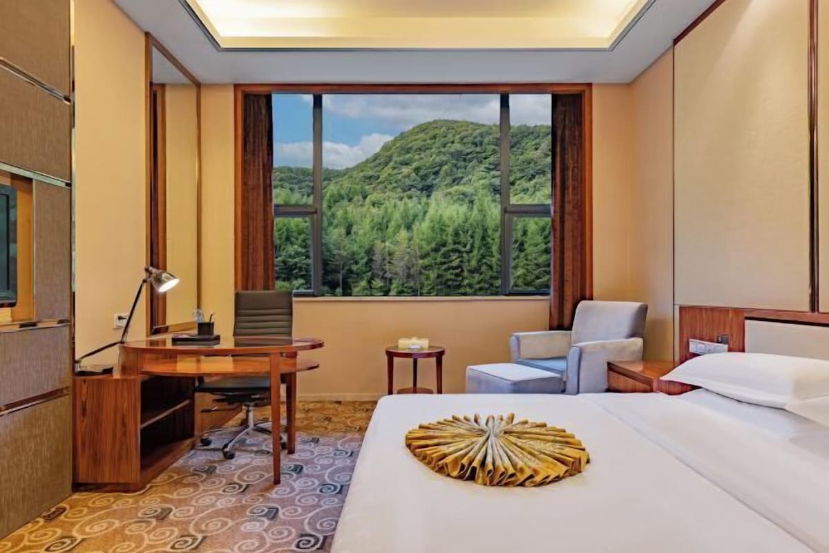 Habitación de hotel con cama, escritorio y silla, ventana con vistas a la montaña y una mesita con una vela.
