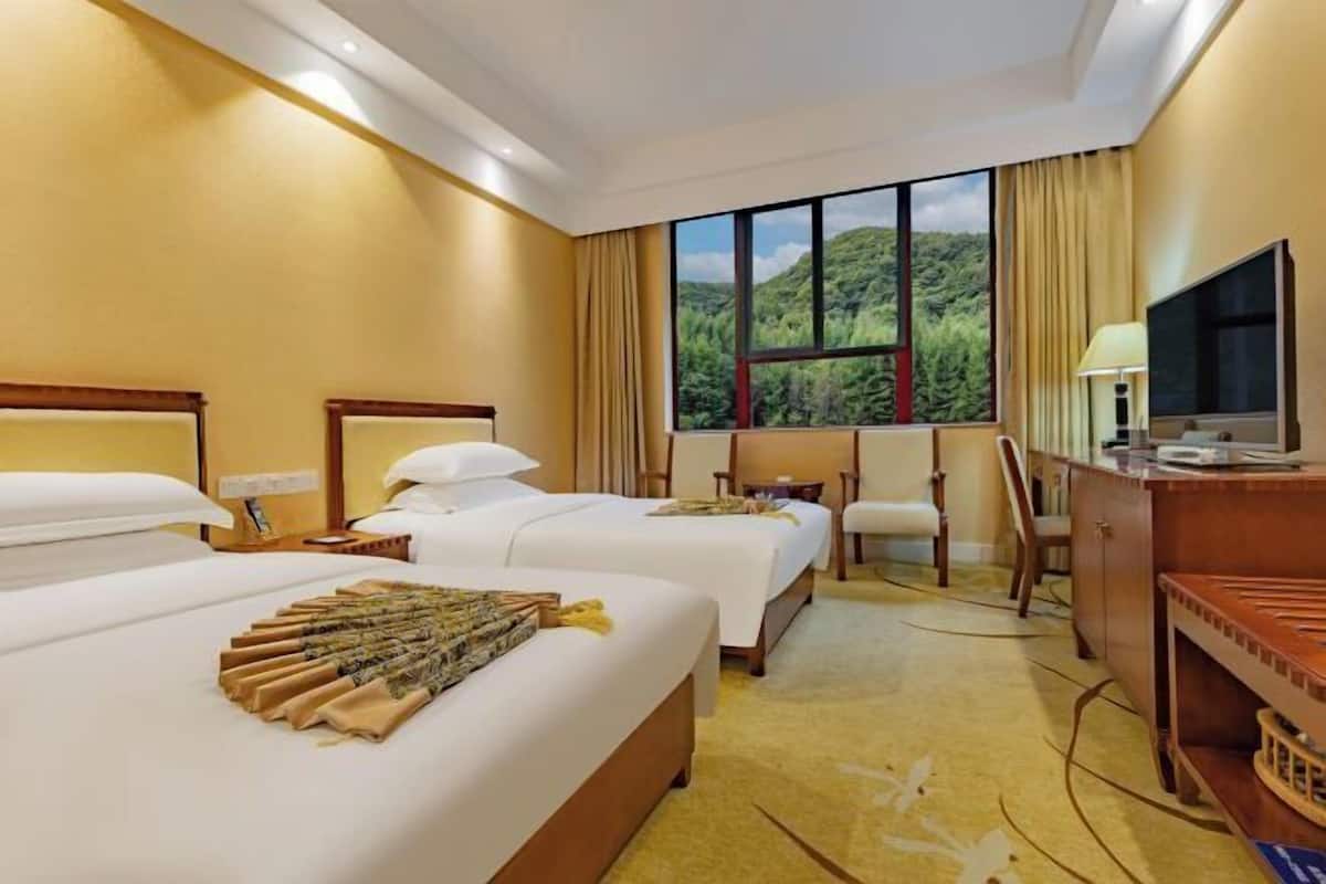 Habitación de hotel con dos camas, un escritorio, una silla, un televisor y una ventana con vistas a zonas verdes.